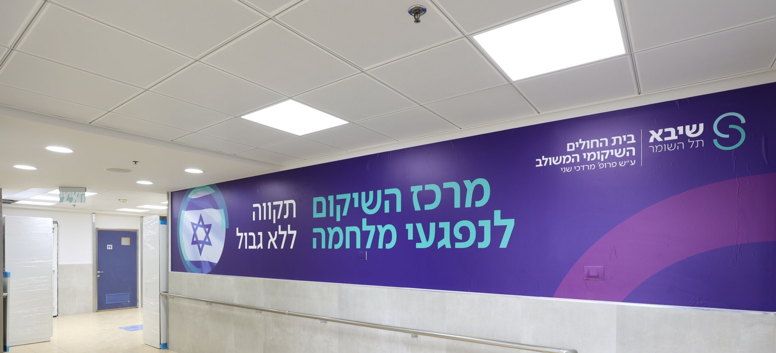 A banner at the Sheba Medical Center with Hebrew writing: "Sheba Tel Hashomer Integrated Rehabilitation Hospital Ayesh Prof. Mordechai Shani Rehabilitation Center for War Victims. Boundless"